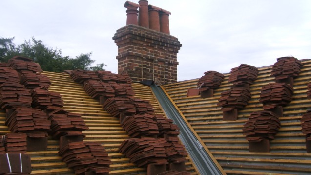 Clay tile roof in progress around a chimney